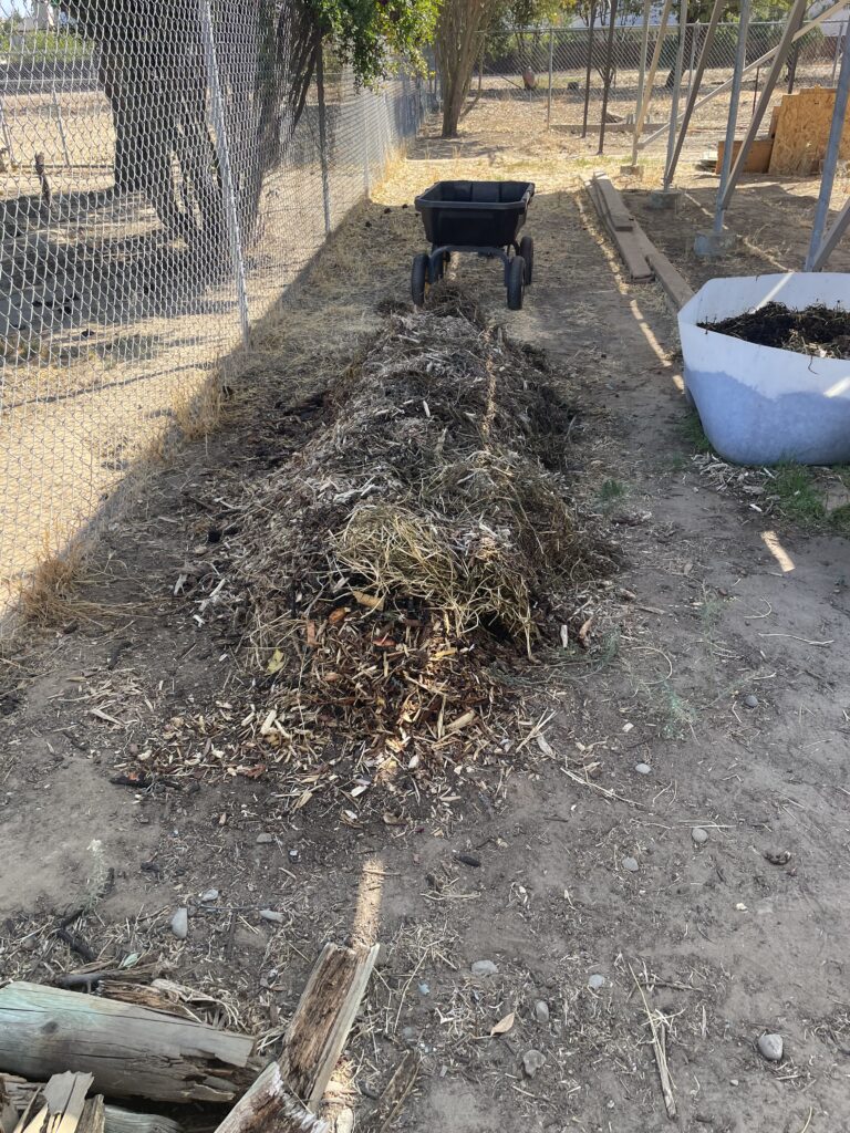 Long row of coarse mulch beside a chain-link fence, with a garden cart behind it.