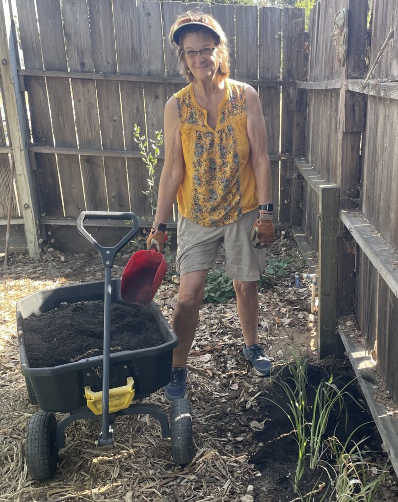 Woman adding compost to a backyard flower garden beside a garden cart
