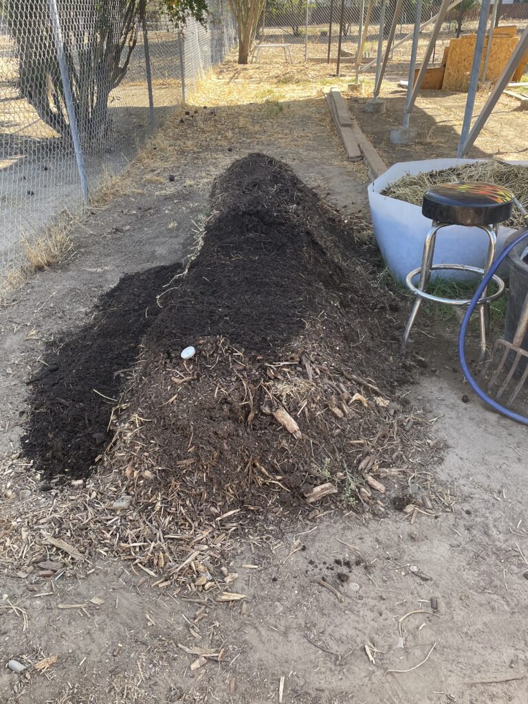 Worm rick with a sleeve of dark material along the fence side and coarse mulch visible at the front.